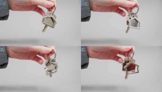 一个女人穿着衬衫的手抖动着金属钥匙链房子的新钥匙的特写镜头。灰色的背景。抵押、租赁和房地产的概念高清在线视频素材下载