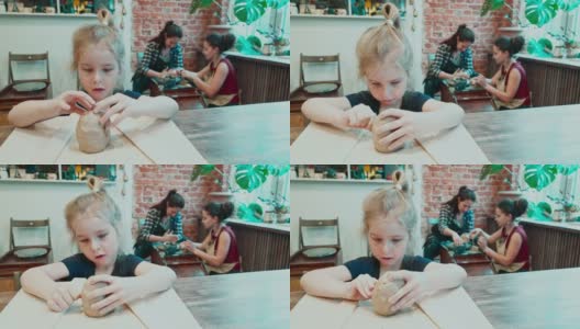 漂亮的小女孩正在用黏土雕刻，而她的妈妈正在一位年轻的女师傅的指导下制作陶器。高清在线视频素材下载