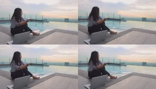 亚洲女性完成了电脑工作，日落时分在豪华酒店摩天大楼的无边游泳池里放松，压力得到了缓解，对项目的完成感到满意，任务按时完成高清在线视频素材下载