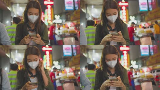 亚洲有吸引力的女人背包客聊天电话，而走在城市。美丽的女游客在街上独自旅行时戴着口罩，在夜间用智能手机与朋友交流。高清在线视频素材下载
