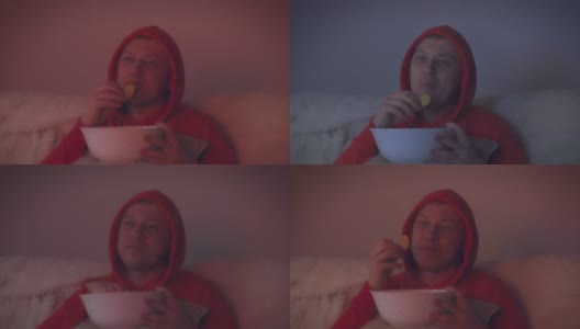 戴兜帽的男人在晚上看一部有趣的电影，用大碗吃薯片高清在线视频素材下载