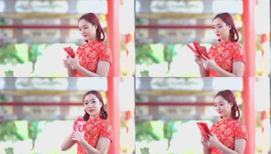 亚洲年轻女子，穿着红色的中国传统旗袍装饰，拿着红色的旗袍信封，上面写着中文的祝福是一个好运气的中国新年快乐高清在线视频素材下载