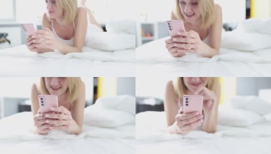 微笑的女人一边躺在手机上一边看手机高清在线视频素材下载