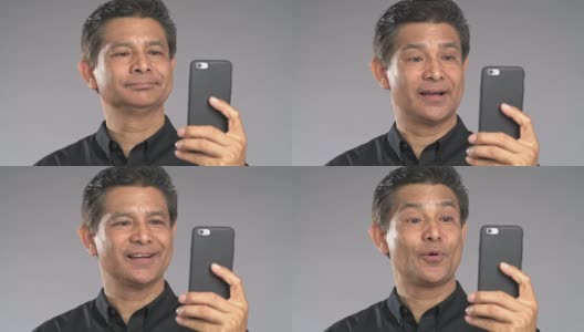 近景老人用手机视频通话，笑脸，孤立在灰色背景中。穿着黑衬衫的亚洲人。高清在线视频素材下载