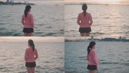 一位美丽的亚洲女跑步者站在沙滩上看海景。高清在线视频素材下载
