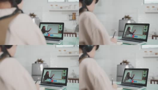 由于冠状病毒大流行，亚洲小女孩通过数字远程互联网会议从学校老师那里学习在线课程。孩子看着电脑笔记本电脑屏幕，那个女人在教书。高清在线视频素材下载
