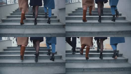 镜头跟随三个穿着秋衣的美丽快乐的女商人的双腿，在寒冷的市中心上楼梯。高清在线视频素材下载