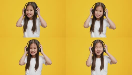 小亚洲女孩听音乐戴耳机，黄色背景高清在线视频素材下载