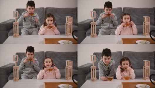白种人的孩子——男孩和女孩，在家里用木砖和木块搭建木结构后，一边喝凉茶，一边休息。精细运动技能开发，益智棋盘游戏概念高清在线视频素材下载
