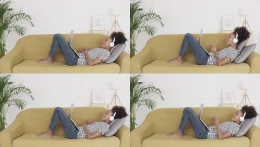 一名非洲妇女躺在家里的沙发上用笔记本电脑进行视频通话高清在线视频素材下载