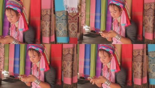 一名妇女穿着传统服装，拿着手机在村里织布高清在线视频素材下载