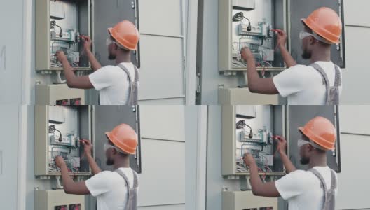 非裔美国电工，穿着制服，戴着头盔，站在电缆箱旁边，为太阳能电站提供服务。维护、人性化、绿色能源理念。太阳能发电厂技术员高清在线视频素材下载