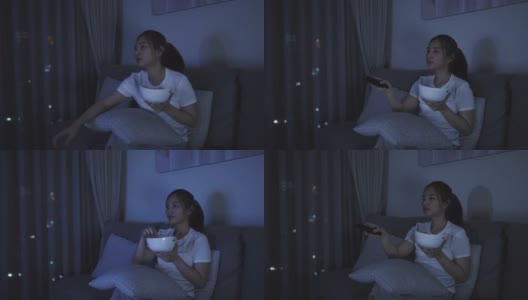 亚洲妇女看电视悬疑电影或新闻看起来快乐和有趣的和吃爆米花在家庭隔离时间在家里客厅沙发深夜。高清在线视频素材下载
