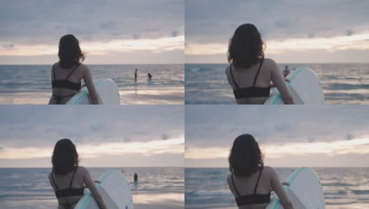 亚洲妇女持有一个sup板和划桨和行走在海滩上。背景是大海和日落。后视图。夏天冲浪。高清在线视频素材下载