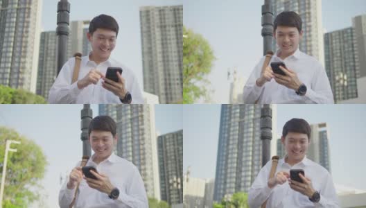一位面带微笑的亚洲商人站在城市外的街道上，用智能手机上网。高清在线视频素材下载