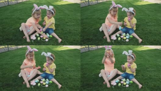 快乐的小妹妹们坐在绿色的草地上玩复活节彩蛋。高清在线视频素材下载