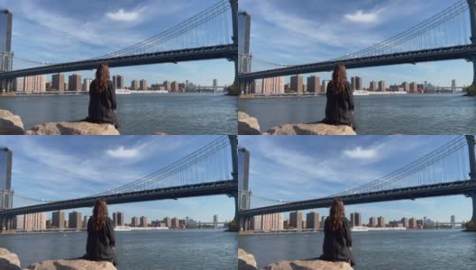年轻美丽的女人坐在堤岸的石头上，在Dumbo，布鲁克林高清在线视频素材下载