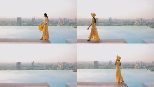 美丽的女人走在池边，穿着黄色的长裙和黄色的帽子。女人们漫步在无边的游泳池旁，伴着夕阳的城市风光。高清在线视频素材下载