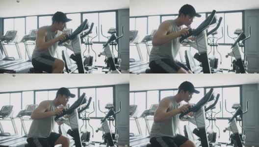 慢动作场景:亚洲青年男子在自行车运动器械上跑步，在健身房锻炼和锻炼有氧运动，以达到运动训练的生活方式理念高清在线视频素材下载