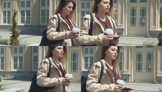 穿着外套的女人在户外散步，手里拿着咖啡和电话高清在线视频素材下载