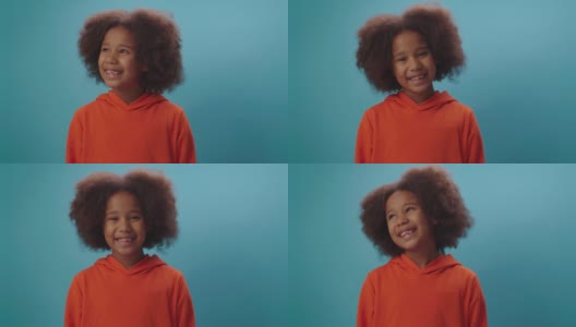 微笑的非裔美国女孩的肖像在橙色的衣服看着镜头在蓝色的背景。7岁快乐小孩的特写。高清在线视频素材下载
