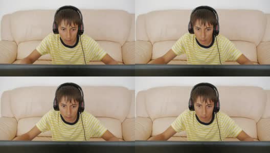 青少年使用笔记本电脑。沉迷于视频游戏的青少年用耳机粘在笔记本屏幕上按键盘。高清在线视频素材下载
