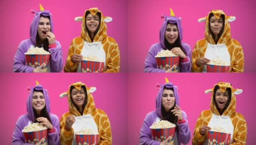 两个穿着独角兽和长颈鹿睡衣的女人一边吃着爆米花一边看喜剧高清在线视频素材下载