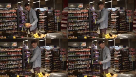 一名身穿蓝色衬衫的白人男子在一家超市的农产品部购买水果和蔬菜。拿起柚子，放进黑色的提篮里，再往前走。大杂货店高清在线视频素材下载
