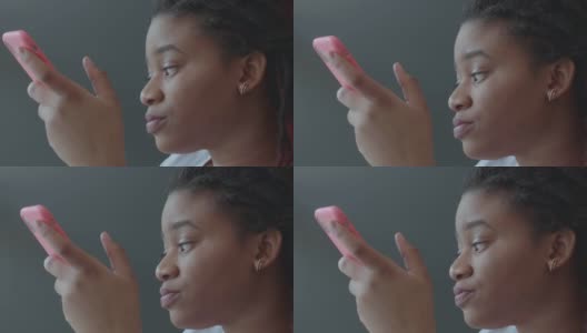 一名留着非洲式发型的女子坐在咖啡馆的桌子旁，一边思考，一边用粉色手机壳装着智能手机高清在线视频素材下载