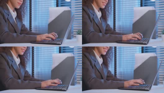 拉美裔美丽的商业女人微笑的特写，而工作在办公室。穿着正装的漂亮的职业女性员工坐在办公室的桌子上，用笔记本电脑打字。高清在线视频素材下载