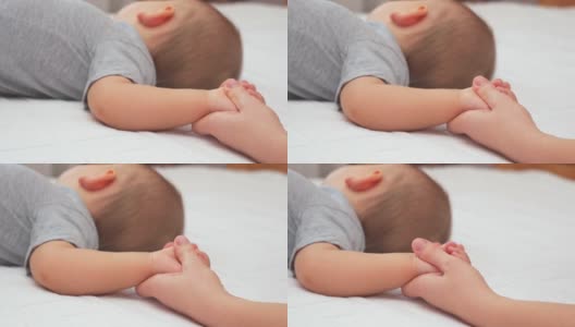 妈妈握着熟睡的婴儿的手掌，轻轻地抚摸着他，镜头从左向右移动高清在线视频素材下载
