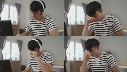 疲惫的亚洲男子成年学生脱下耳机，揉着疼痛的眼睛，白天在卧室的电脑上学习。高清在线视频素材下载