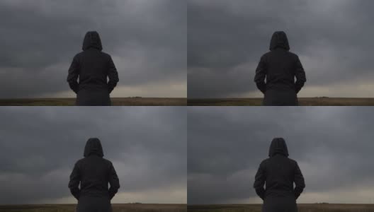 背影的女性穿着连帽夹克对抗黑暗忧郁戏剧性的云在天空高清在线视频素材下载
