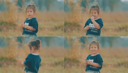 一个微笑的亚洲可爱女孩的肖像看着相机和闻到草地上的花高清在线视频素材下载