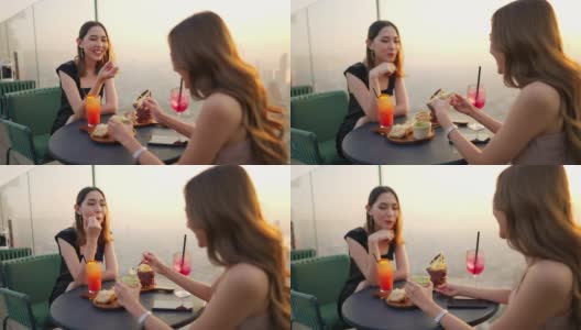 4K亚洲女性朋友在夏日夕阳下在摩天大楼的屋顶餐厅共进晚餐。高清在线视频素材下载