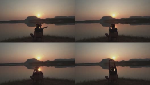 ฺ背影一个年轻人和休息在河边的山景日落。高清在线视频素材下载
