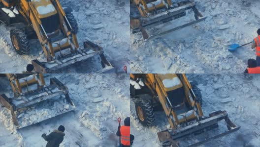 道路工人用铲子从路上铲雪，一辆拖拉机用铲斗收集并运走冰块。清扫冬季道路上的积雪。工作中的道路服务。高清在线视频素材下载