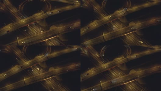 夜间的高速公路上，无人机从上到下拍摄了经过桥梁和高架桥的十字路口的汽车。高清在线视频素材下载