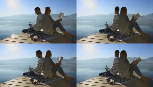 一对年轻夫妇带着书、平板电脑在湖边码头休息高清在线视频素材下载