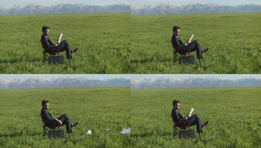 一位商人坐在田野里的办公椅上高清在线视频素材下载