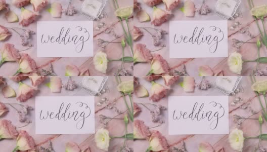 一张大理石桌子上的婚礼卡片，旁边是粉红色的花朵，俯视图放大高清在线视频素材下载