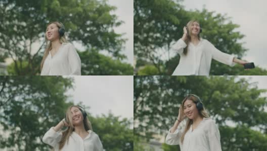 美丽年轻的亚洲女性跳舞旋转户外和有乐趣戴耳机听音乐在一个阳光明媚的日子在大自然呼吸新鲜的空气。高清在线视频素材下载