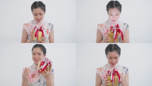 中国/亚洲妇女打开她手中的一个金色的大礼盒，她从她的家人，亲戚和朋友为新年的快乐，在中国的春节，穿着旗袍白色的衣服高清在线视频素材下载