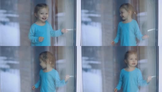一个有着蓝色眼睛的小女孩和她美丽的妈妈坐在窗台上，看着窗外的乡村小屋的冬天高清在线视频素材下载