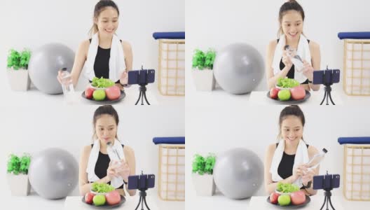 美丽的亚洲女人健康的博主展示了苹果水果和干净的减肥食品。在智能手机前录制视频直播在家。在线社交媒体上的健身影响者。高清在线视频素材下载