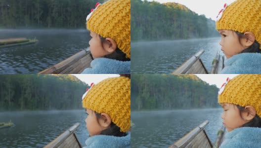 一个可爱的小女孩在竹筏上通过雾漂浮在湖面上在早上，在泰国Mae Hong Son高清在线视频素材下载