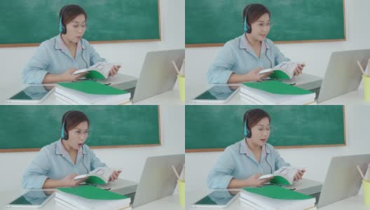 亚洲女教师通过视频会议为学龄前儿童大声朗读课本，在教室里用笔记本电脑和黑板进行电子学习。在家教育和远程学习，在线，教育和互联网。高清在线视频素材下载