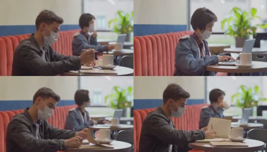 镜头从一名年轻的亚洲女子用笔记本电脑工作，喝着咖啡，到一名男子坐在咖啡馆的桌子上用笔记本做笔记，两人都戴着口罩高清在线视频素材下载