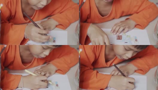 穿着橙色衬衫的小男孩正在纸上画画。高清在线视频素材下载