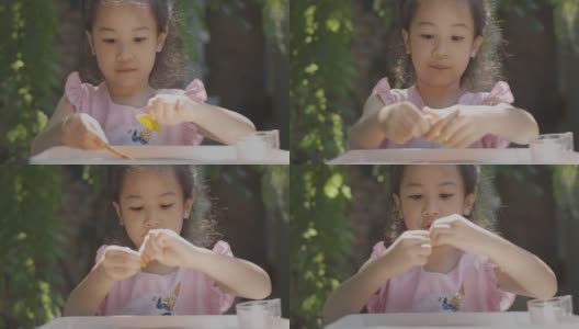 靠近可爱的亚洲小女孩的美丽的脸，坐在户外阳光下玩耍，展示了在家儿童休闲活动的概念，表达快乐，乐趣和快乐的情感。高清在线视频素材下载